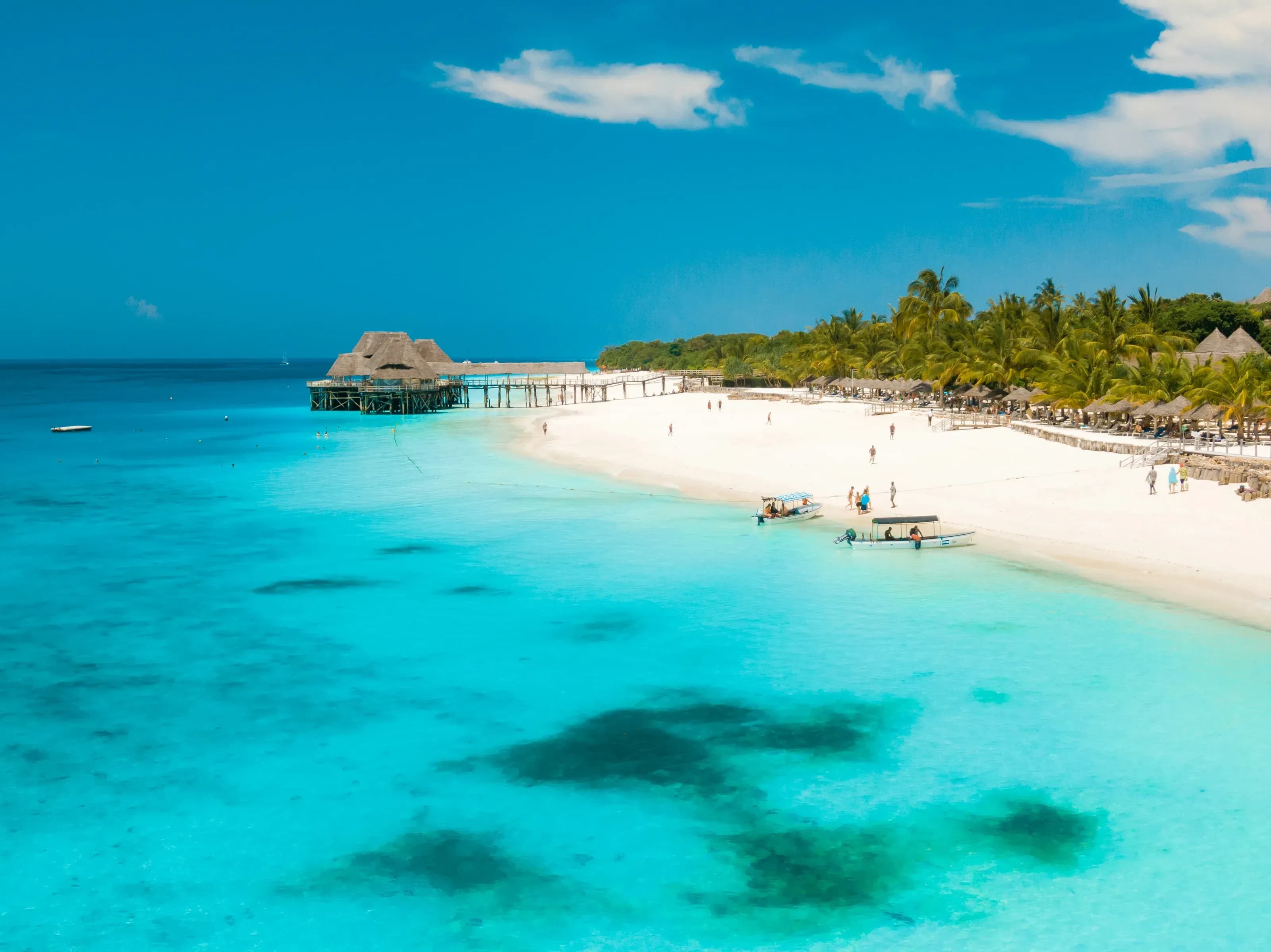 A thatched jetty restaurant standing over turquoise shallows beside a white sand bay.