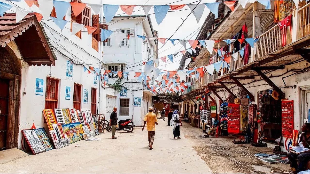 A Stone Town street strung with bunting, paintings for sale along one wall and stalls along the other.