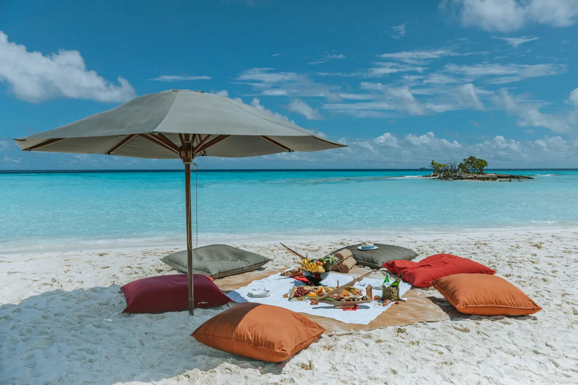 A shaded picnic laid out on white sand beside turquoise shallows.
